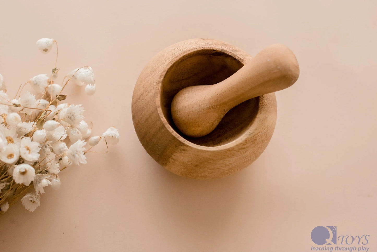 Wooden mortar and pestle on a neutral background with white flowers.