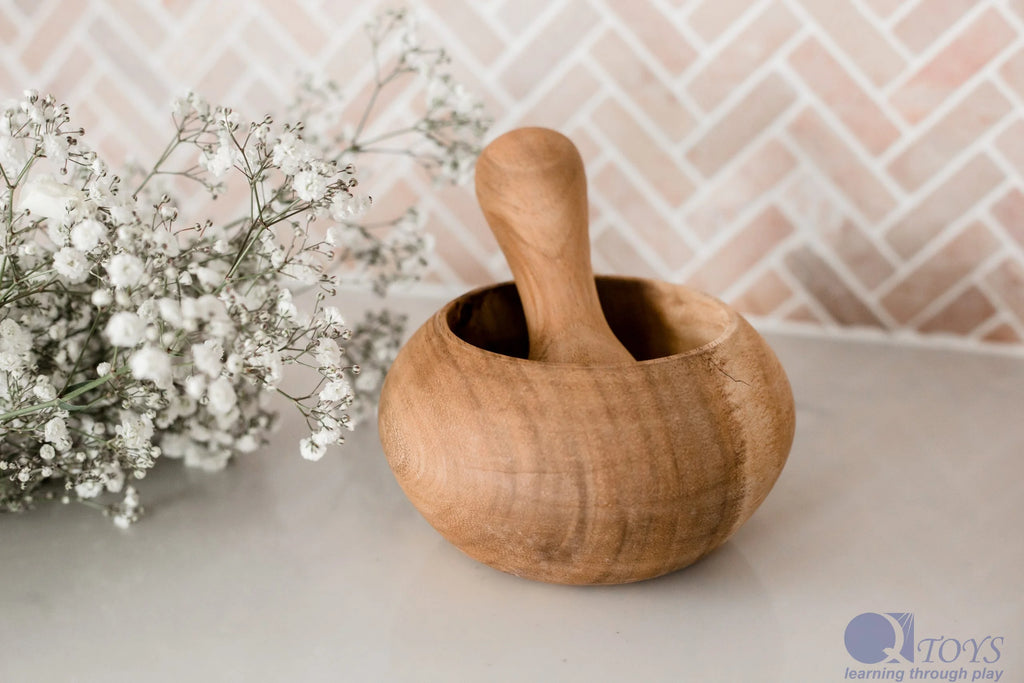 Wooden mortar and pestle on a neutral background with baby's breath flowers.