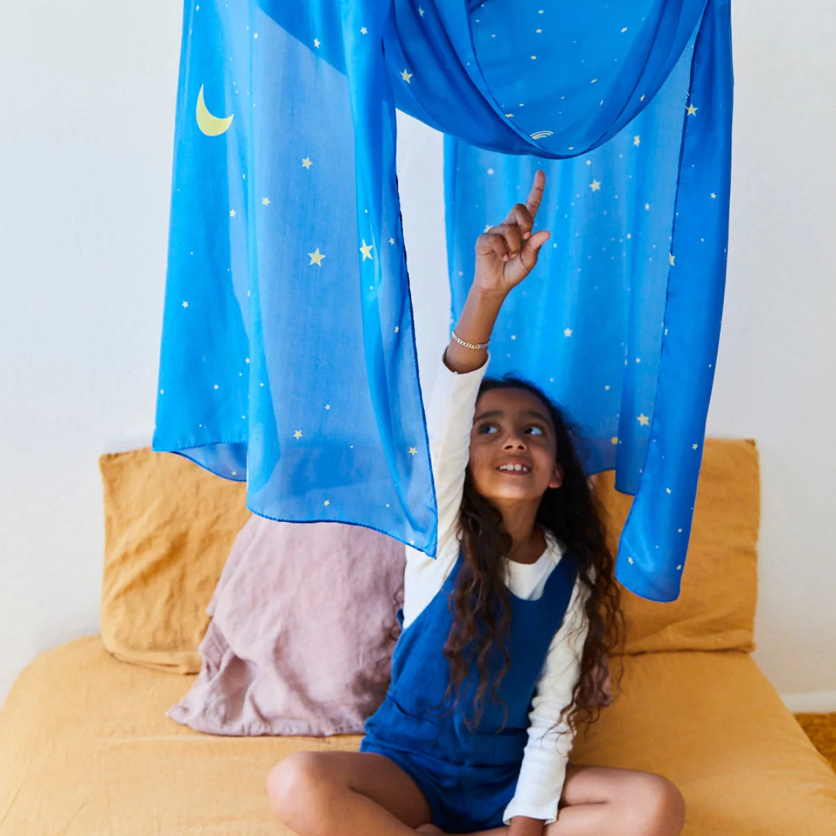 Blue play silk with stars and moon hanging above bed with child pointing to it.