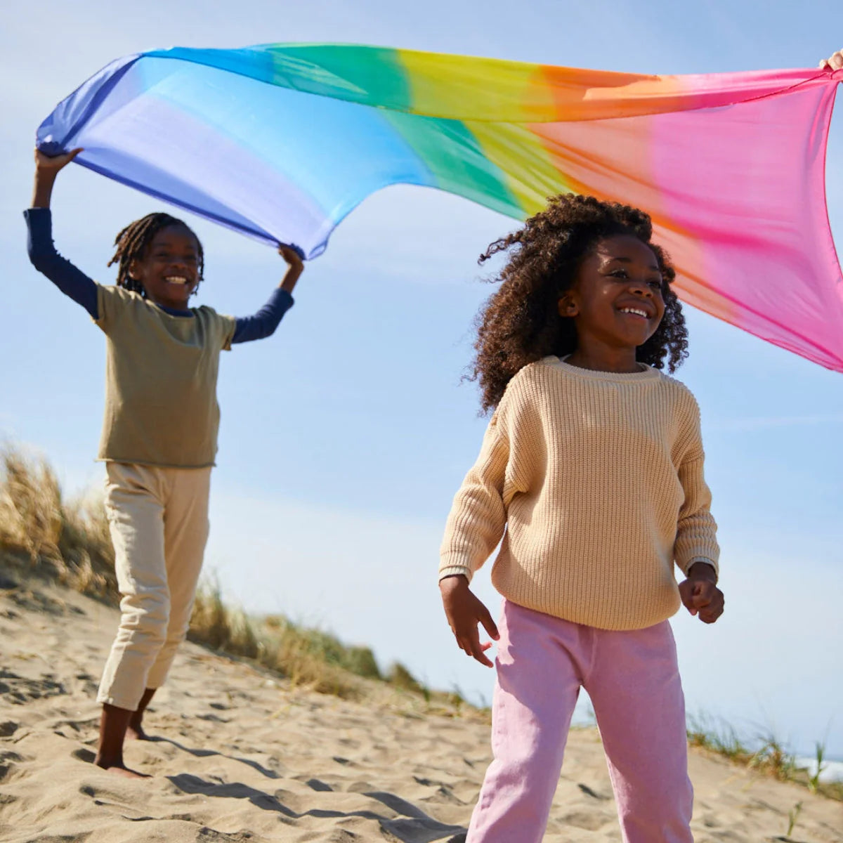 Two children playing on a beach with a colourful playsilk.