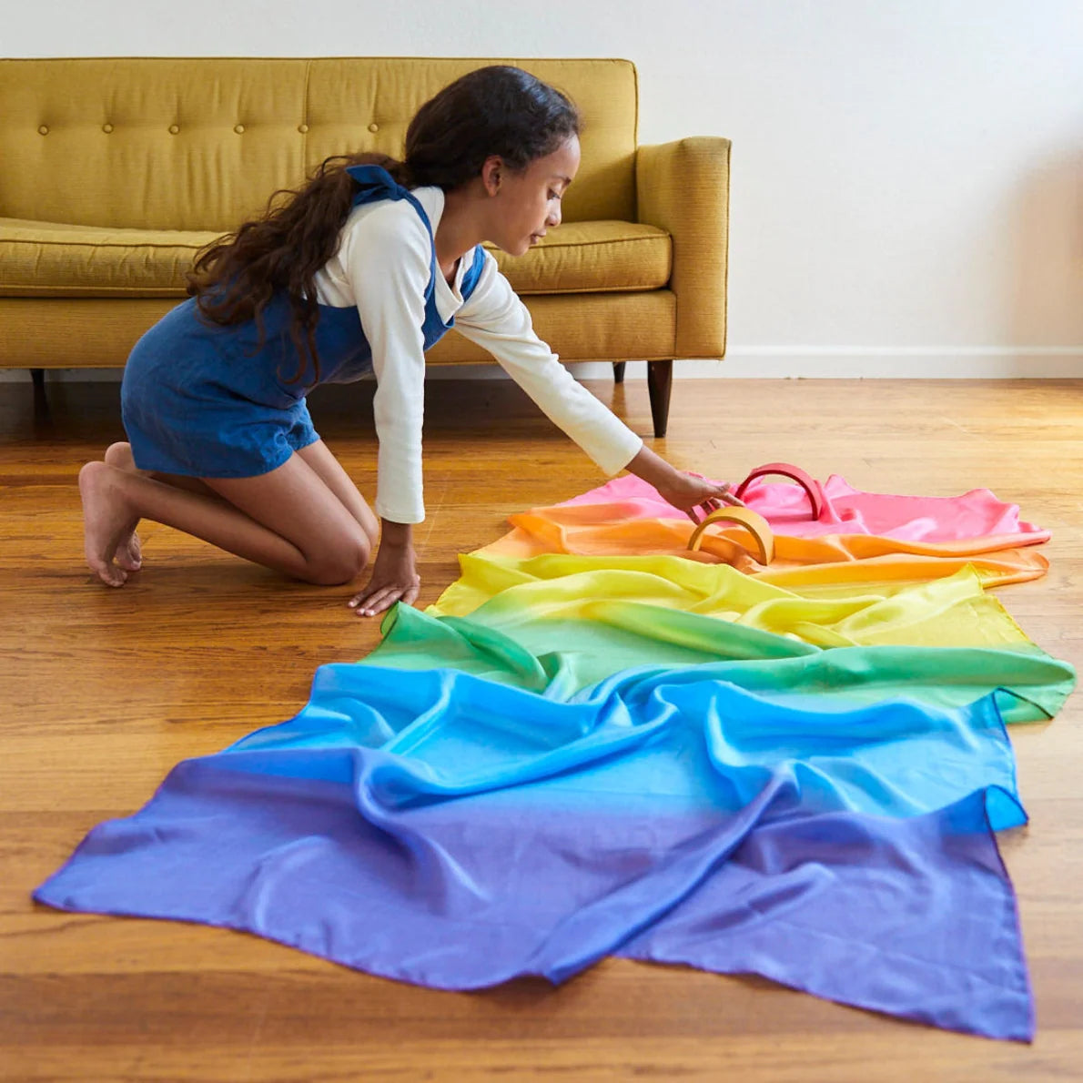 Rainbow play silk on floor with child playing with wooden blocks on it.