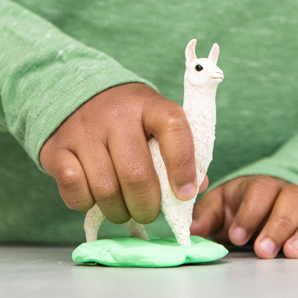 Child's hand holding a toy llama over a green playdough surface