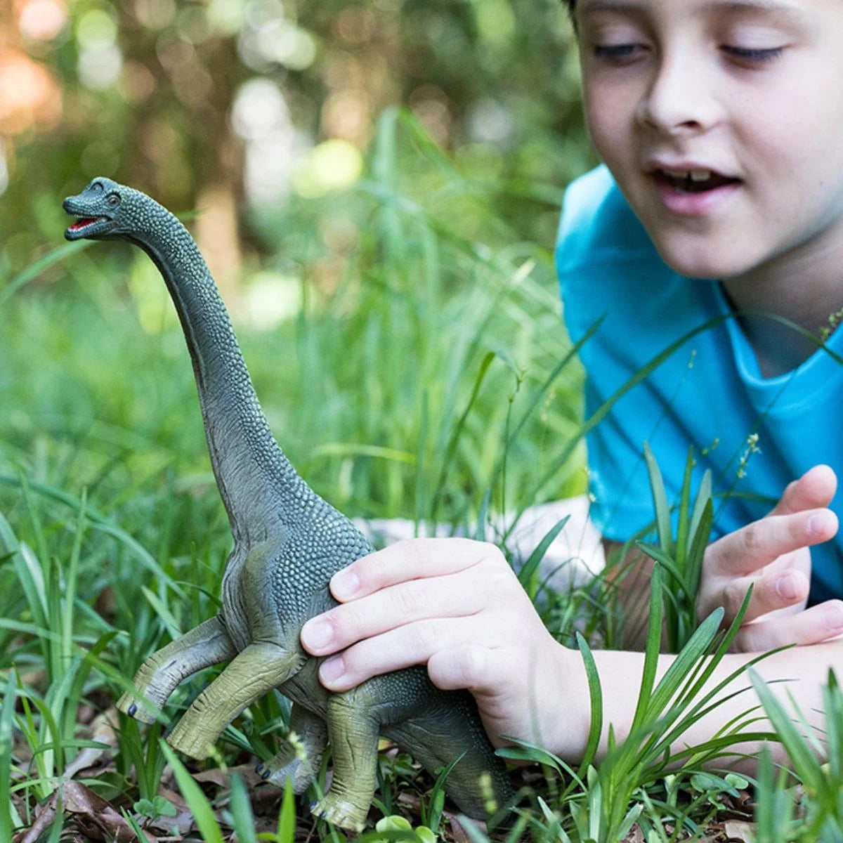 Child holding a toy dinosaur in a grassy outdoor setting