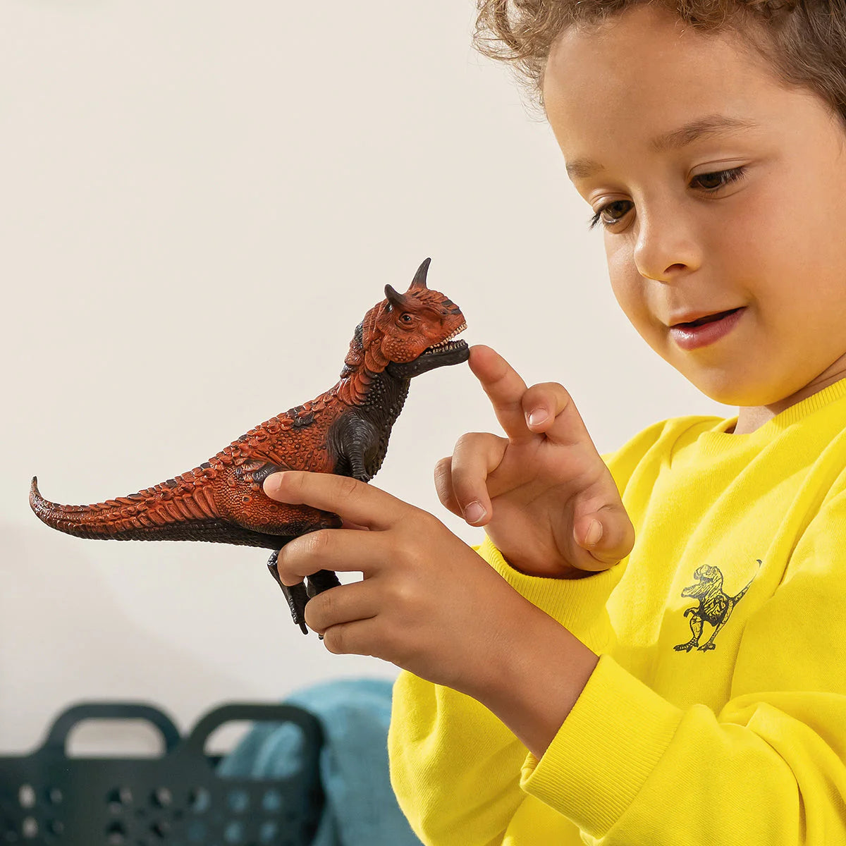 Child holding a toy dinosaur and pointing at it with a yellow shirt featuring a dinosaur design.