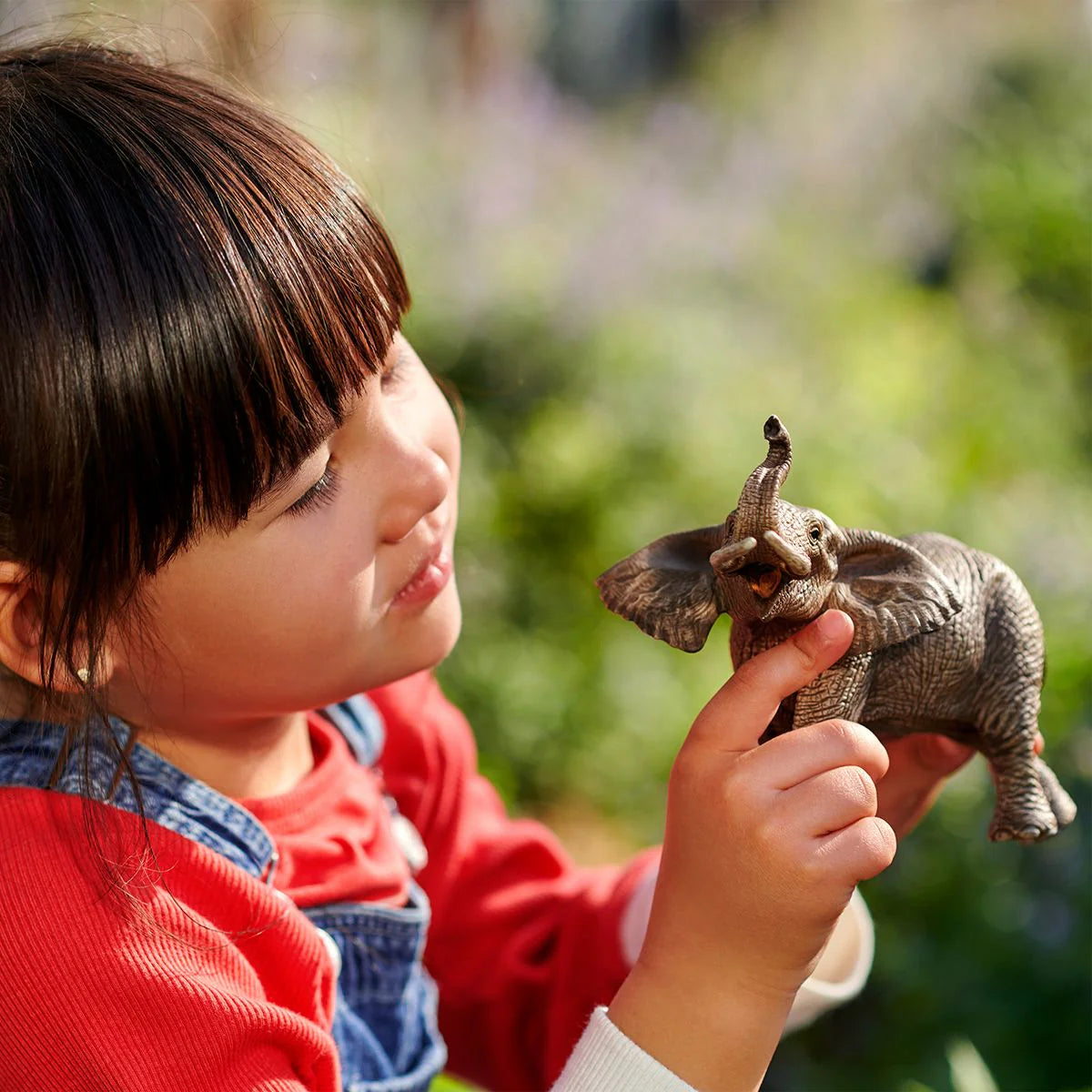 Child holding a toy elephant outdoors with greenery in the background