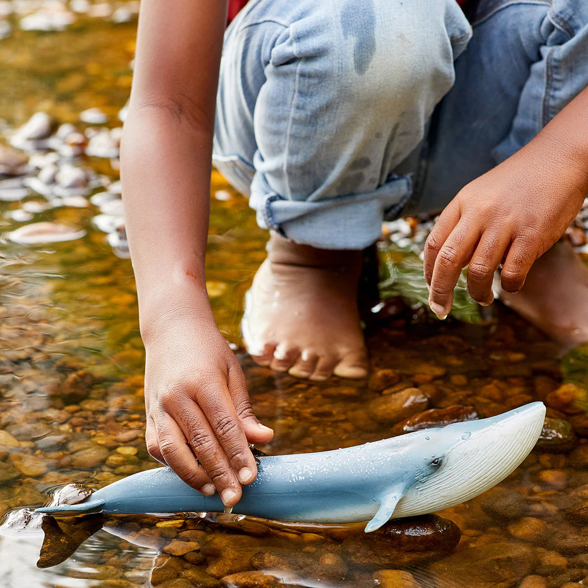 Child holding a toy whale in a stream