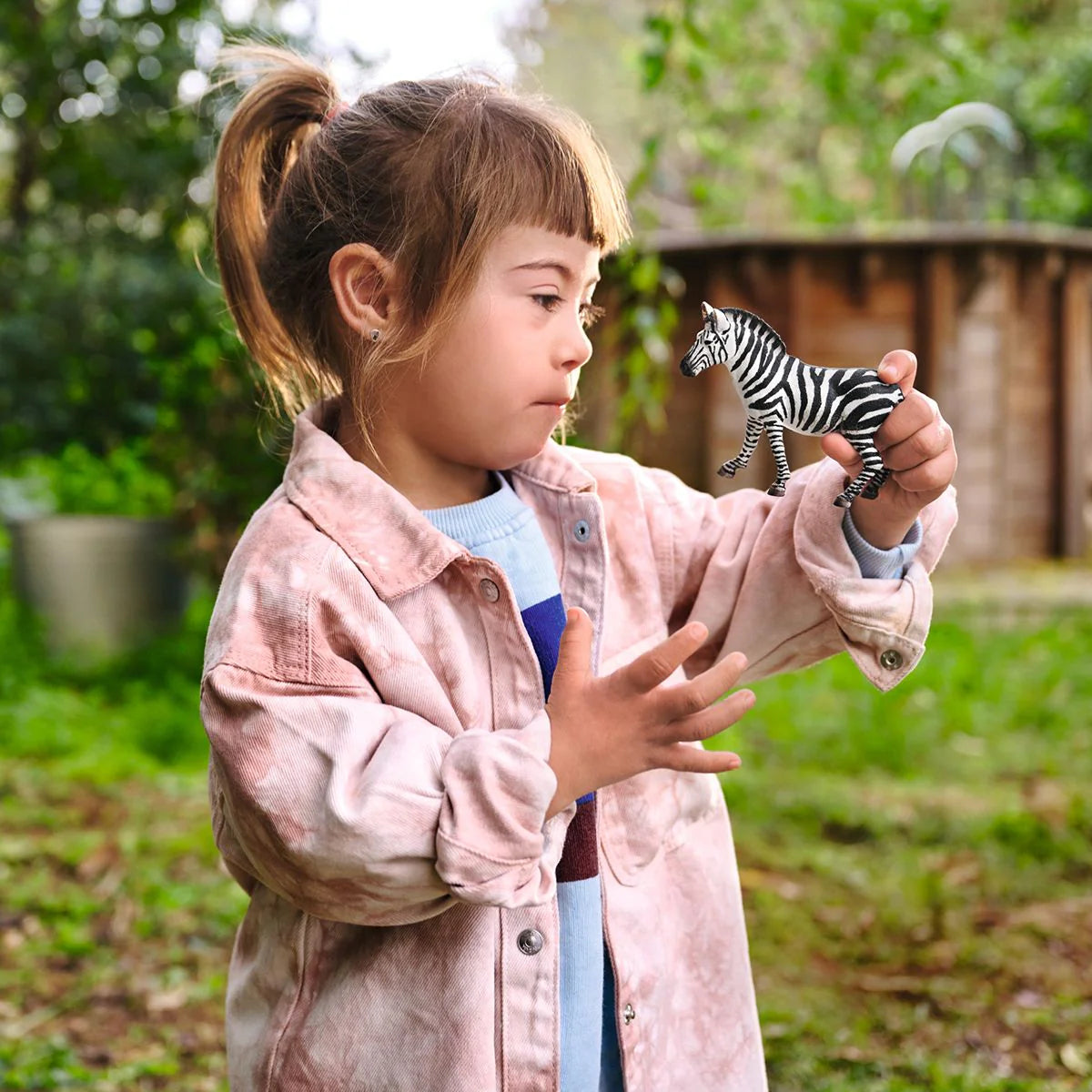 Child holding a zebra toy outdoors with greenery in the background