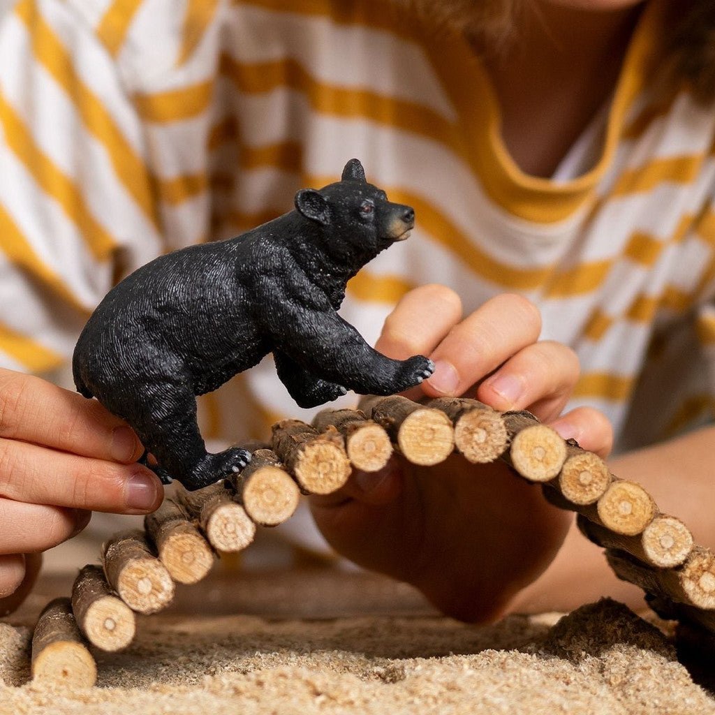 Person playing with a black bear figurine on a wooden bridge