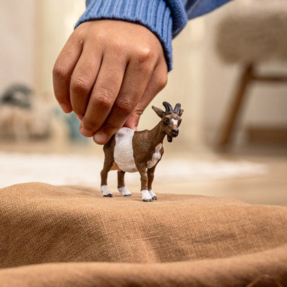 Hand holding a small goat figurine on a textured surface