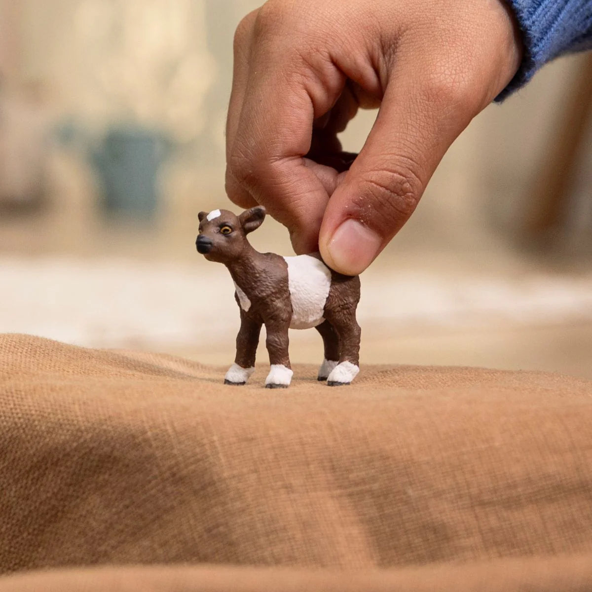 Small goat figurine held by a hand on a textured surface