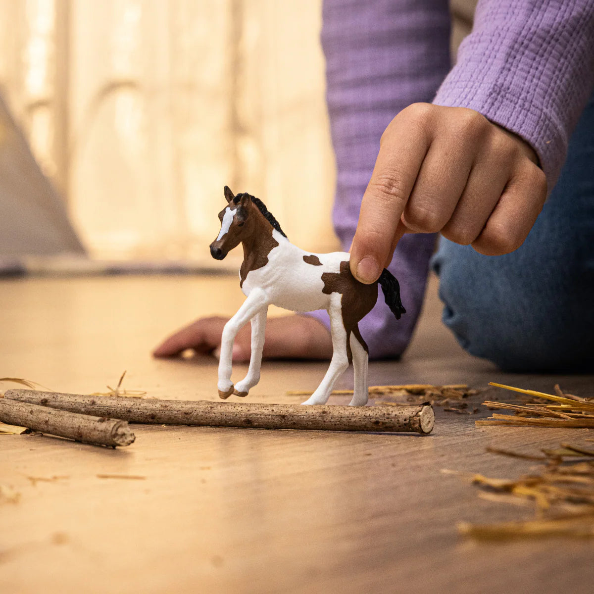 Hand holding a toy horse on a wooden surface with blurred background