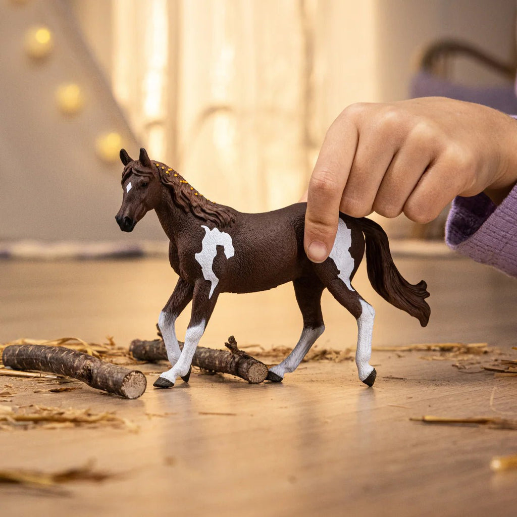 Toy horse being held by a hand on a wooden surface with blurred lights in the background