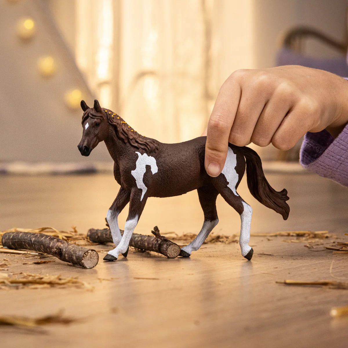 Toy horse being held by a hand on a wooden surface with blurred lights in the background