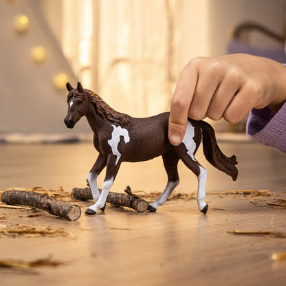 Toy horse being held by a hand on a wooden surface with blurred lights in the background