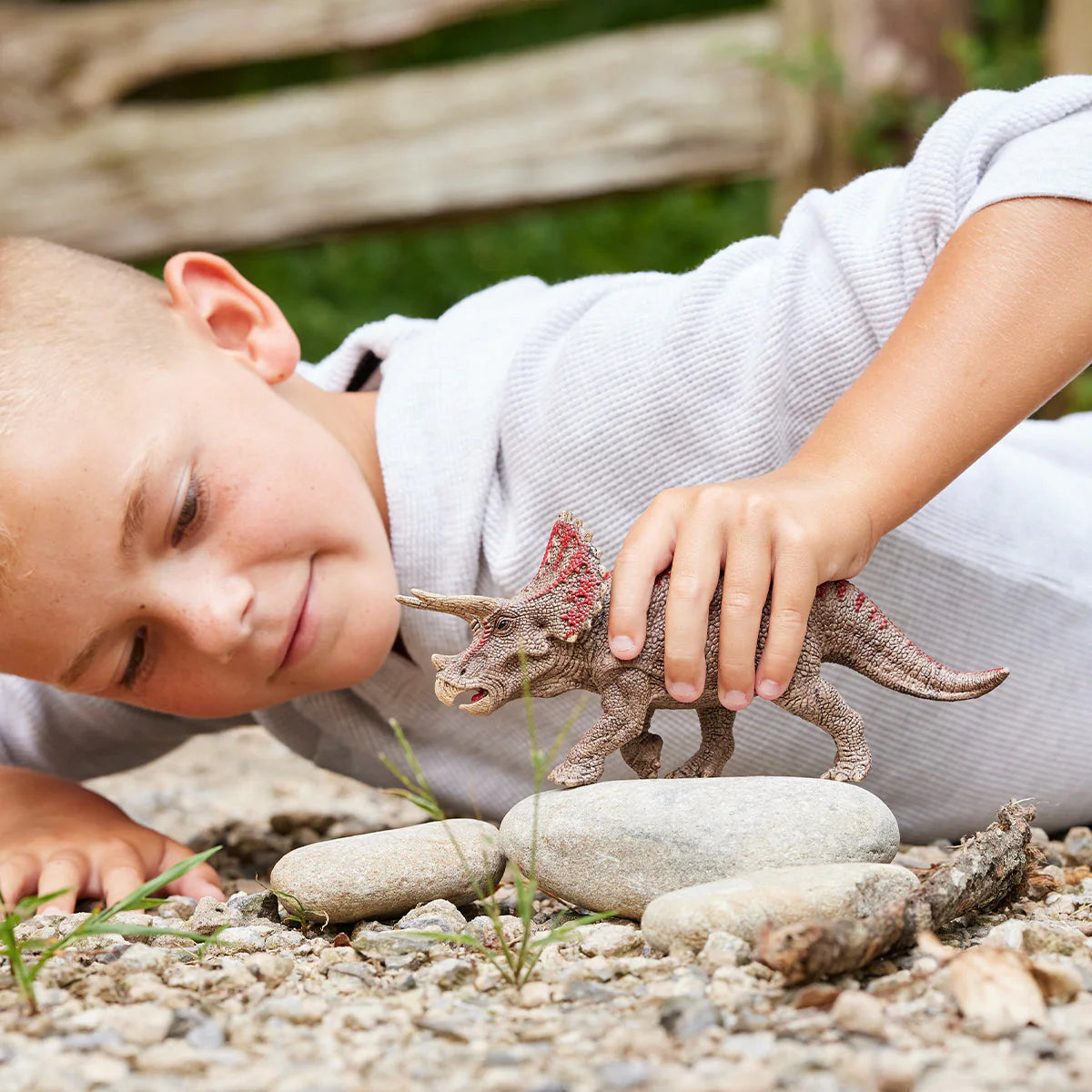 Child playing with a toy dinosaur on a rocky surface
