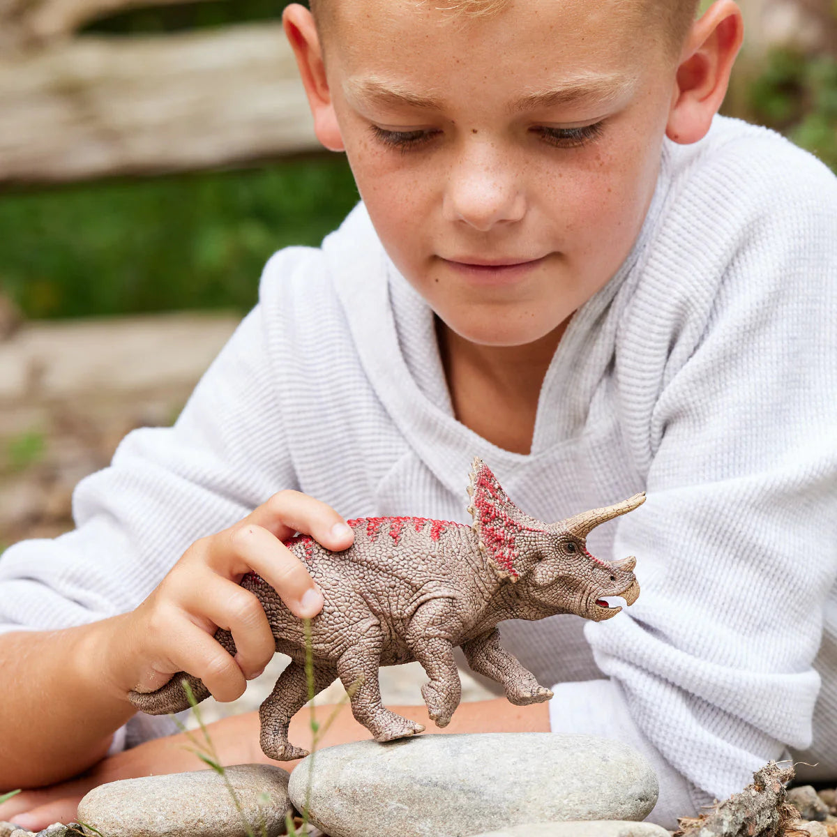 Child playing with a toy dinosaur outdoors