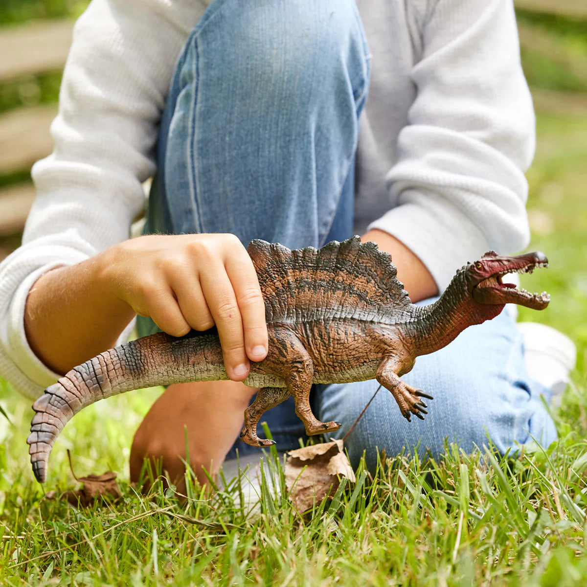 Person holding a toy dinosaur in a grassy outdoor setting