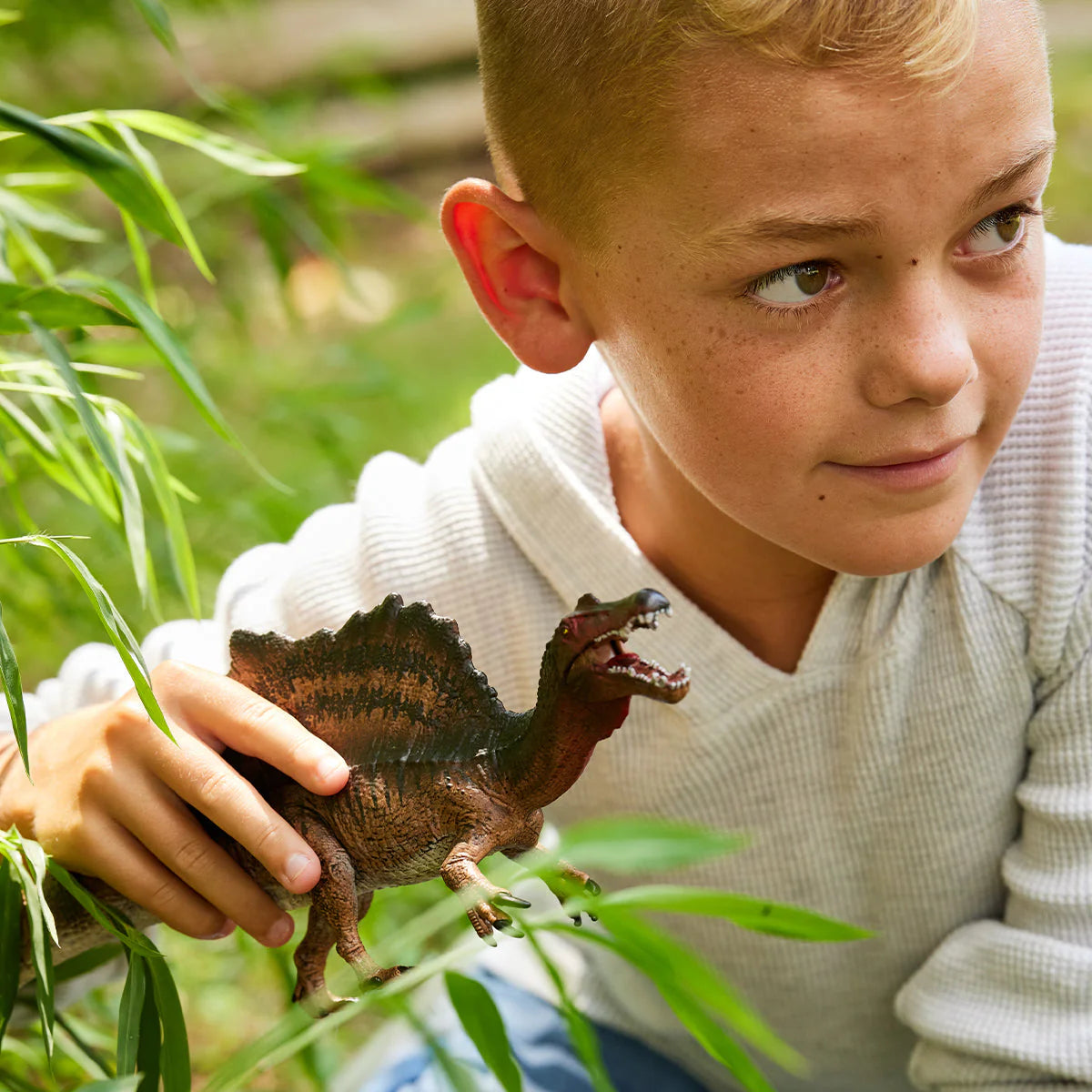 Child holding a toy dinosaur in a natural setting