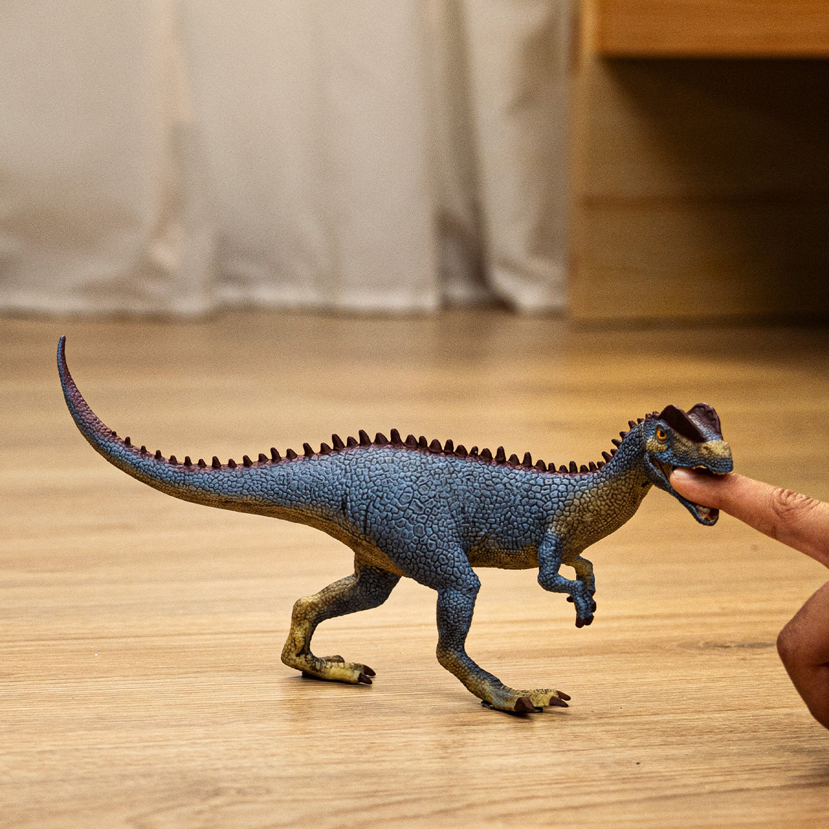 Dinosaur toy being held by a hand on a wooden floor