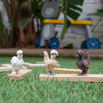Three toy chickens on wooden stands in a grassy area with a blurred background