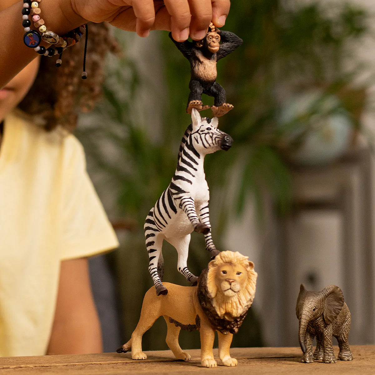 Toy figures of a zebra, lion, and elephant on a wooden surface with a blurred background.