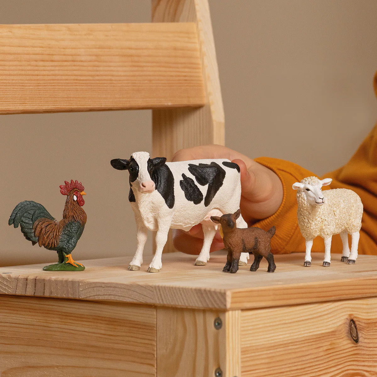 Set of farm animal figurines including a rooster, cow, and sheep on a wooden surface.