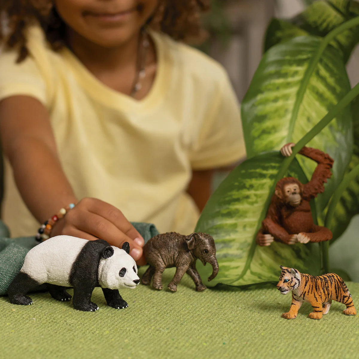 Child playing with animal figurines on a green surface with leaves in the background