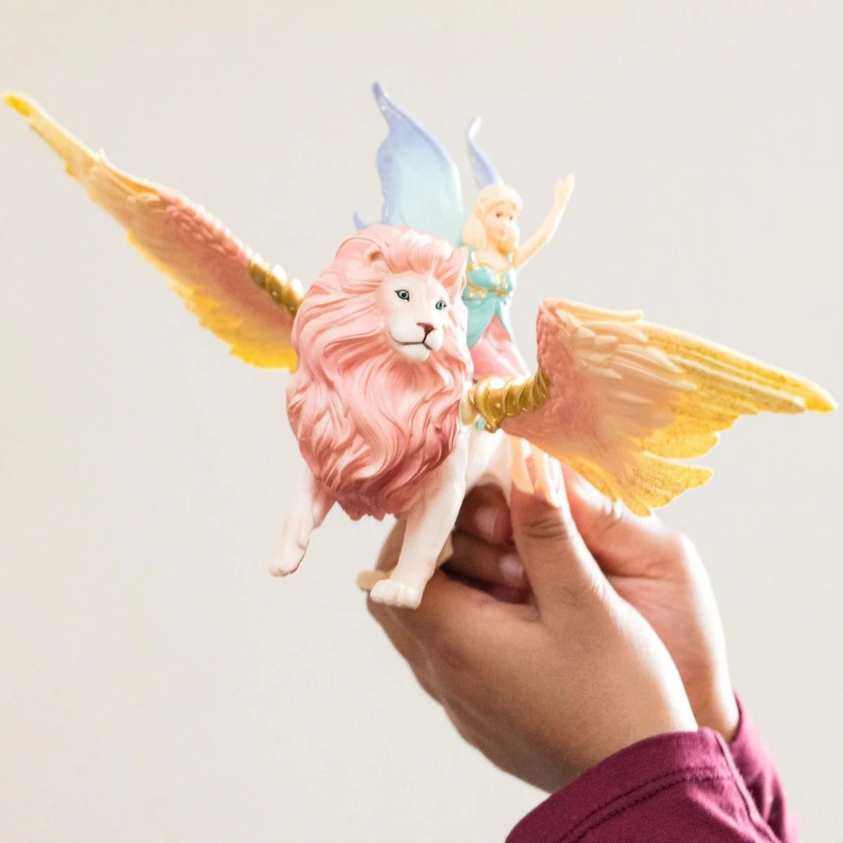 Hand holding a pink lion with fairy wings against a light background
