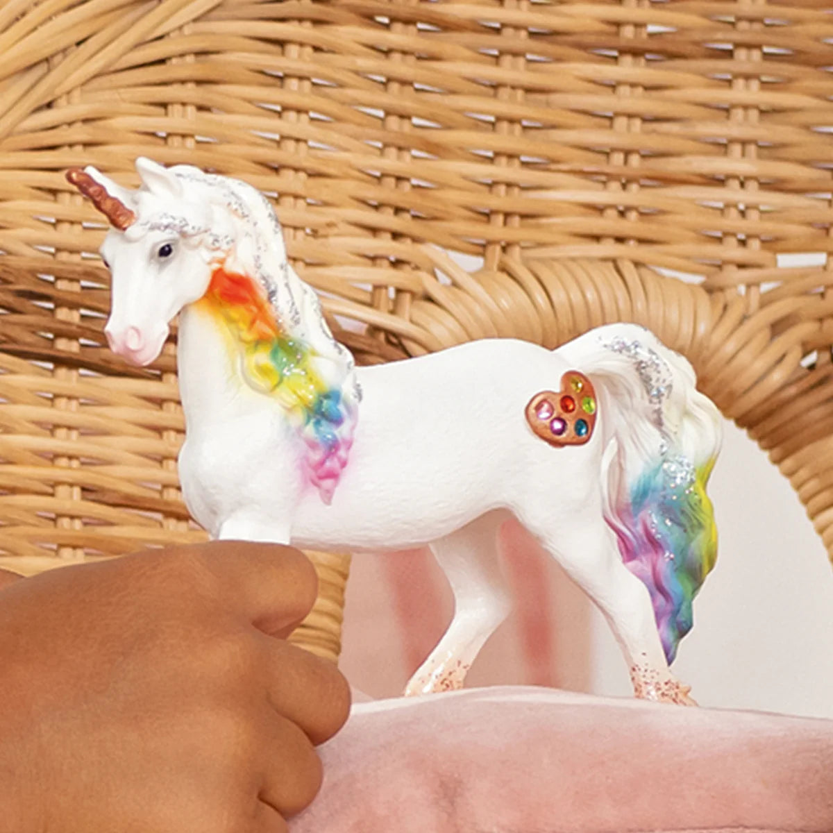 Unicorn figurine with rainbow mane and tail held by a hand against a wicker background