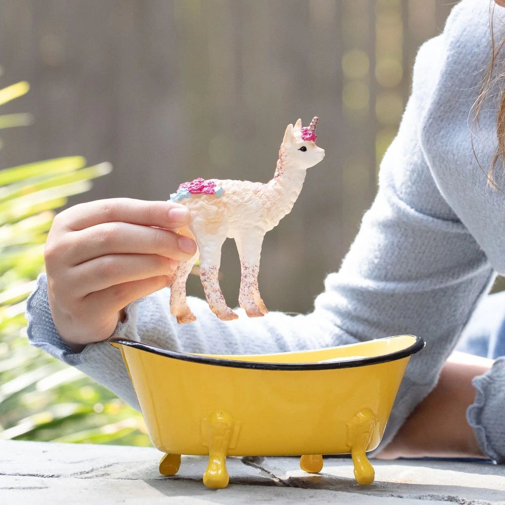 Person holding a small decorative llama figurine over a yellow bathtub-shaped container.