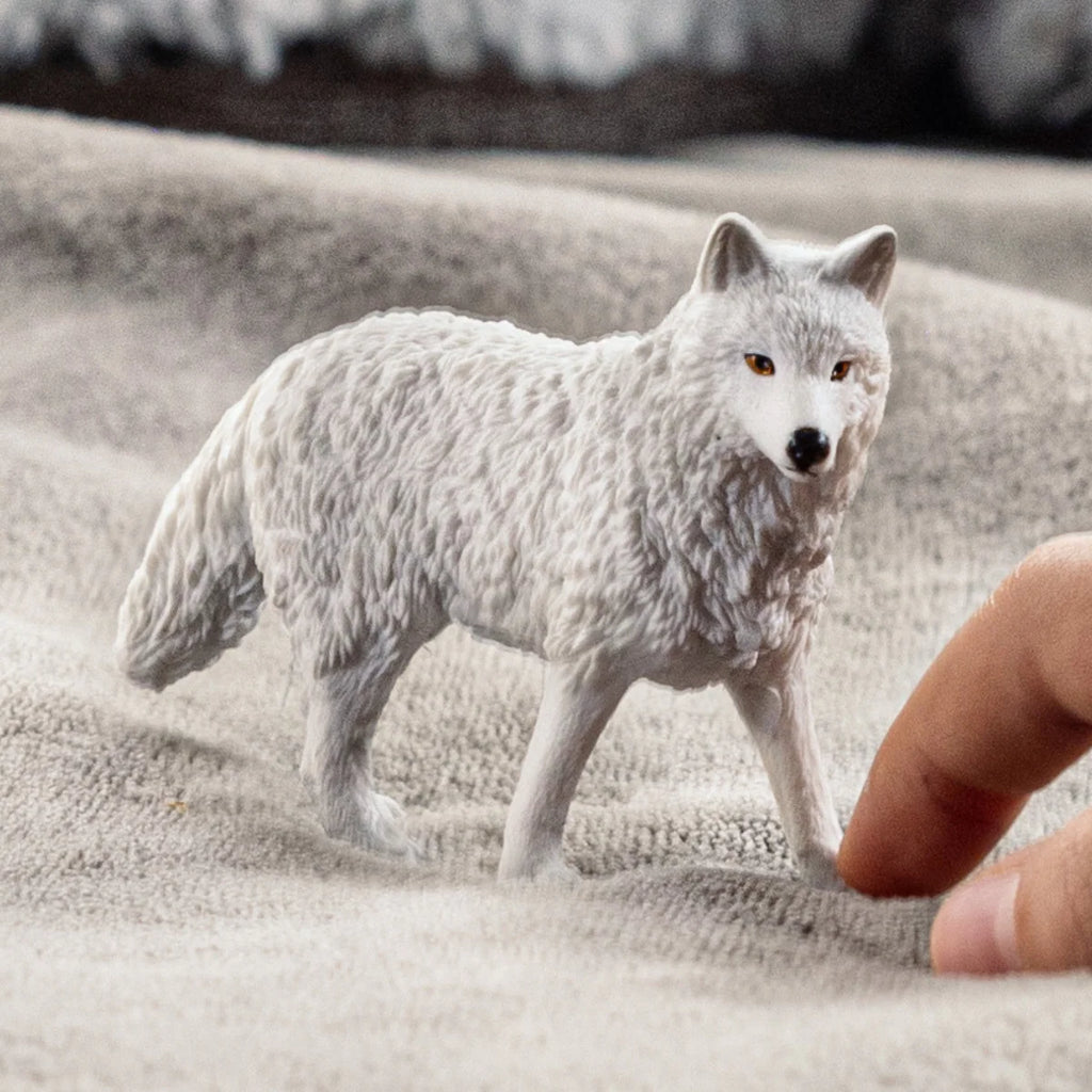 White wolf figurine on a sandy surface with a hand for scale