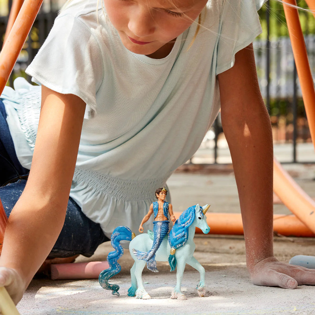 Child playing with toy mermaid and unicorn on a playground