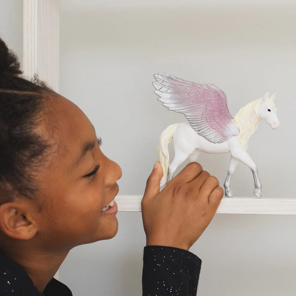 Child holding a toy pegasus figure against a plain background