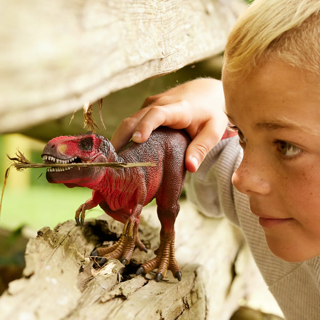 Child playing with a toy dinosaur in a natural setting