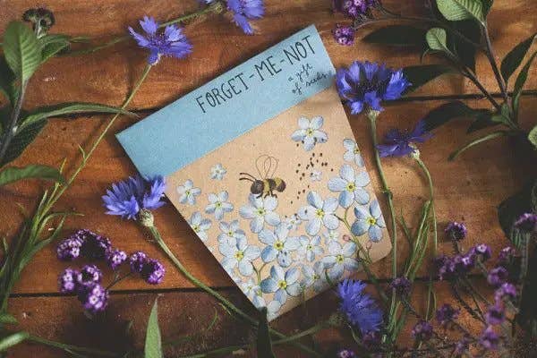 Notebook with floral design and 'Forget-Me-Not' text on a wooden surface with flowers.