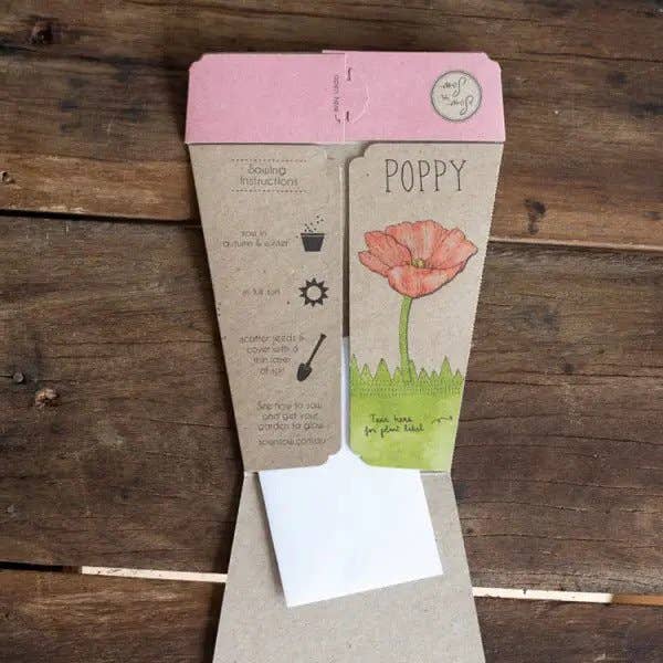 Seed packet with a pink poppy design on a wooden surface