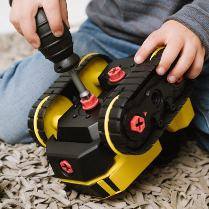 Child playing with a toy drill and construction set on a carpeted floor.