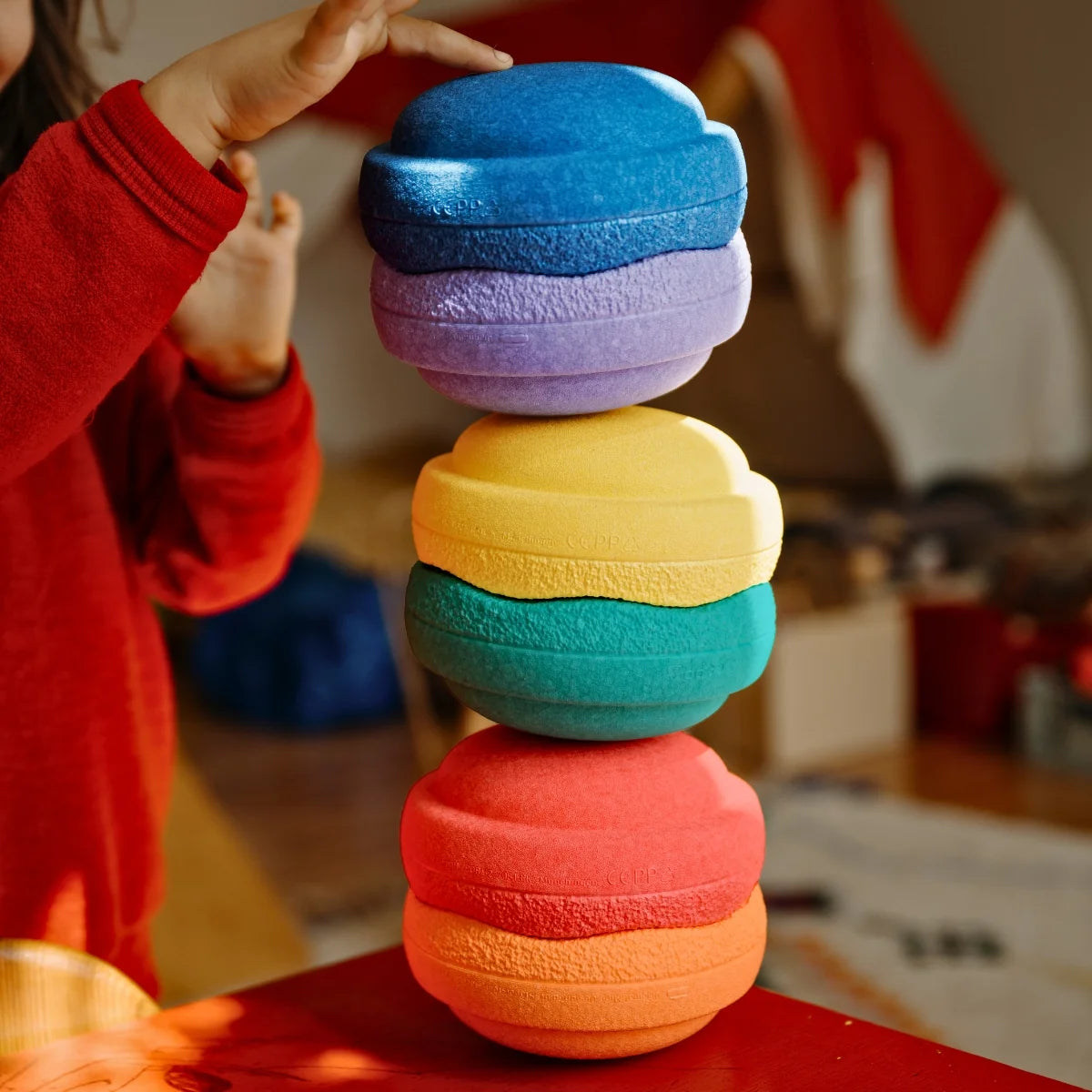 Child stacking colorful rings on a table with a blurred indoor background