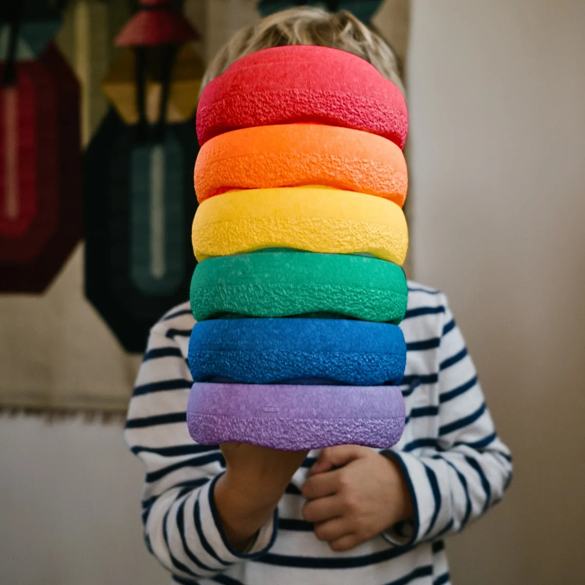 Child holding a stack of rainbow-colored foam blocks.