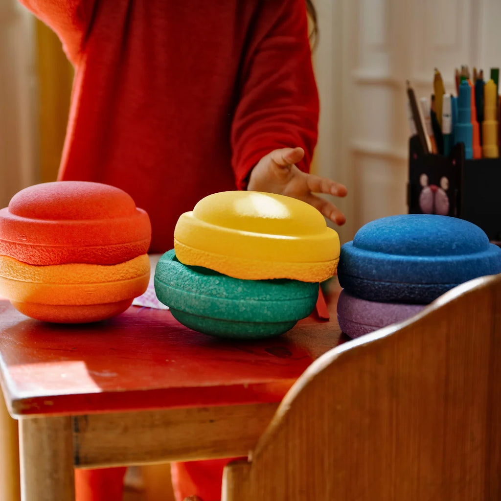 Colorful stacking toys on a child's desk with a child in a red sweater reaching out.
