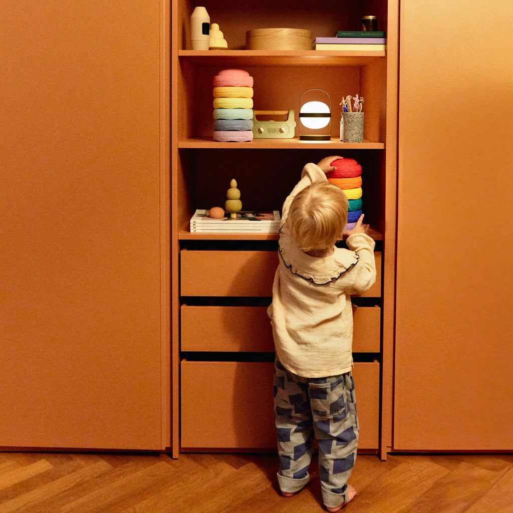 Child playing with colorful toys on a wooden shelf in a room with orange walls.