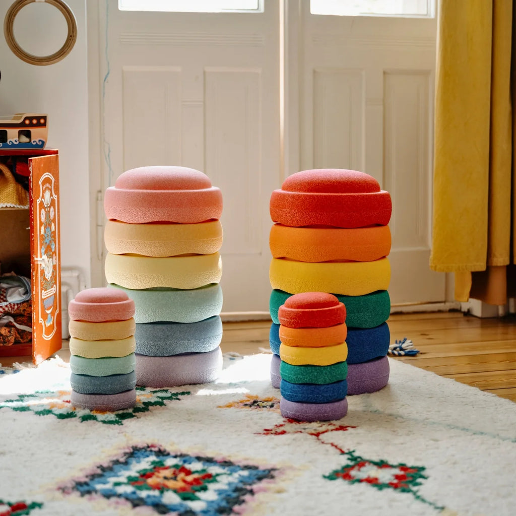 Stacked colorful ottomans on a patterned rug with a yellow curtain in the background.