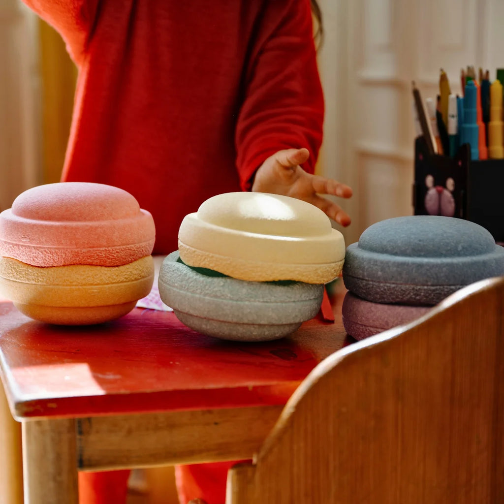 Colorful wooden toys on a child's table with a child in a red sweater in the background.