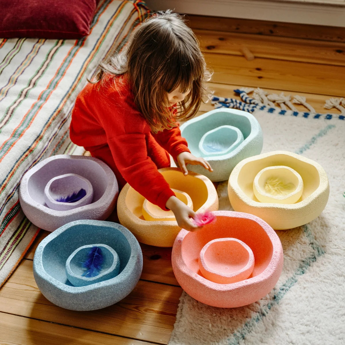 Child playing with colorful foam bowls on a wooden floor