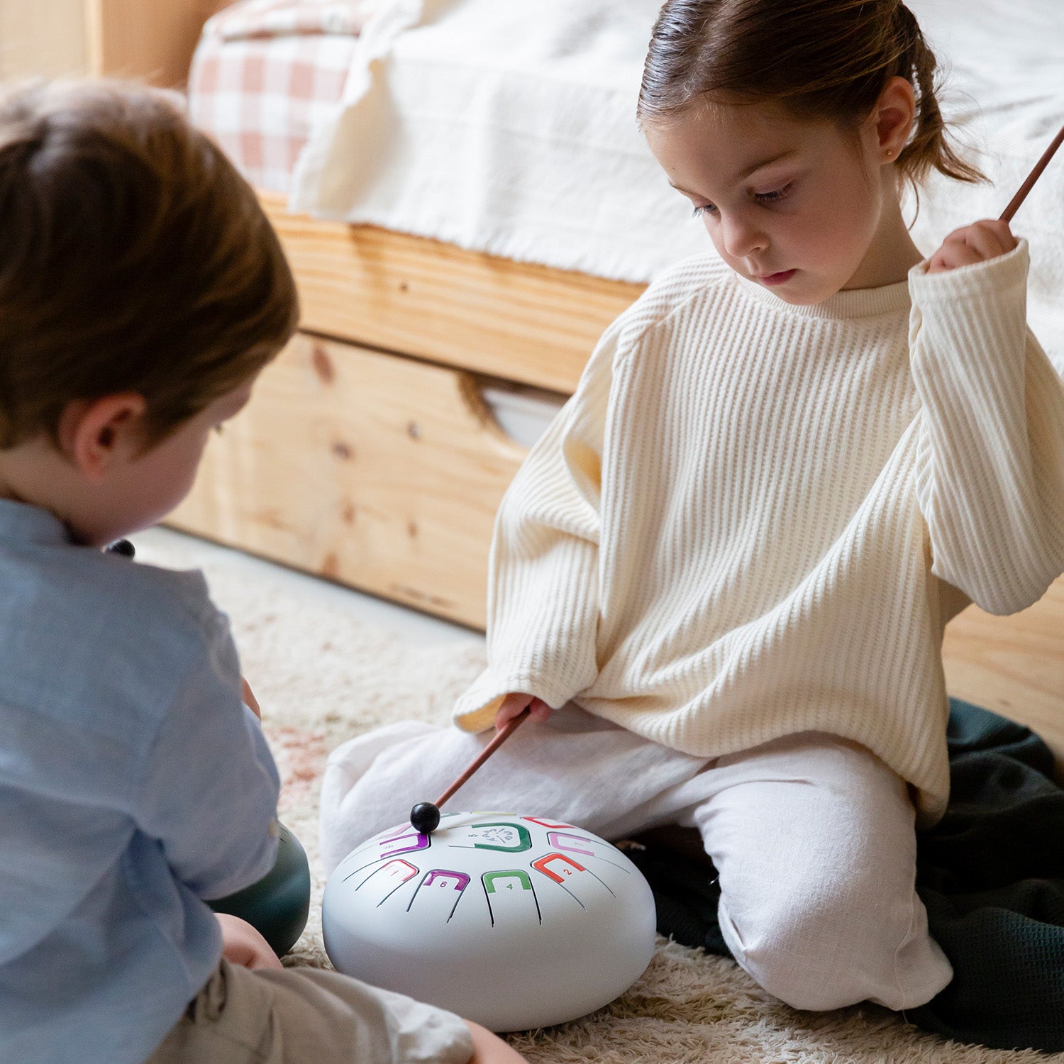 Two children playing with a colorful drum on the floor.