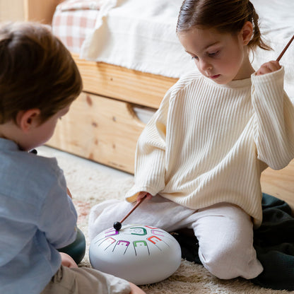 Two children playing with a colorful drum on the floor.