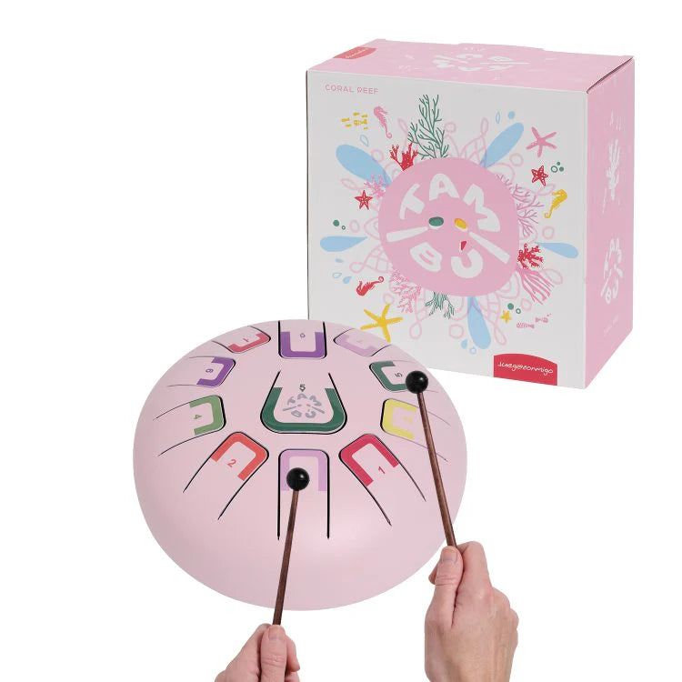 Pink children's metal drum with colorful numbers and letters, held by a hand, with a matching box in the background.