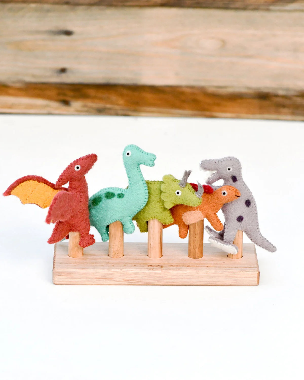 Set of colorful dinosaur figurines on a wooden stand against a wooden background