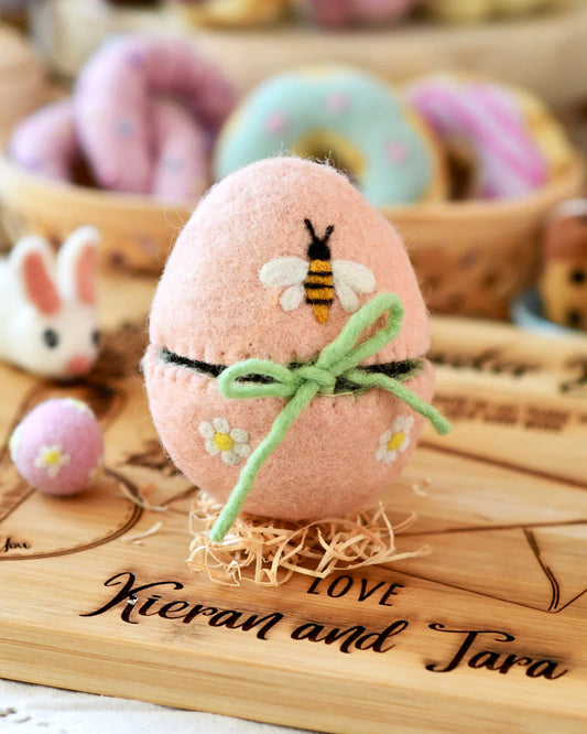 Decorative pink egg with a bee design on a wooden surface.