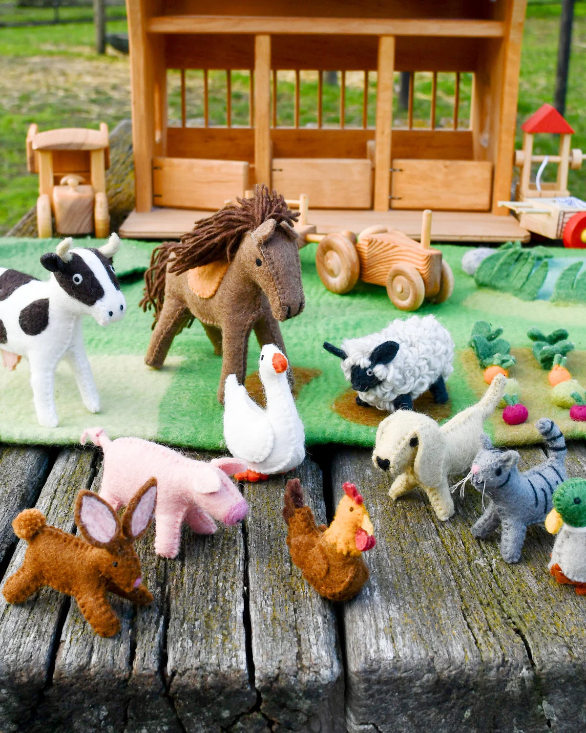 Collection of toy farm animals on a wooden surface with a small wooden barn in the background.